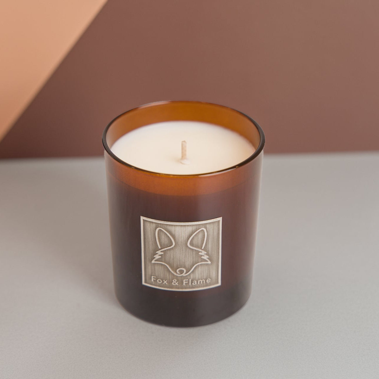 Candle in a brown glass jar with a fox logo on a neutral background