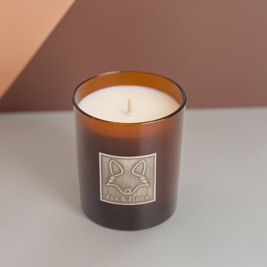 Candle in a brown glass jar with a fox logo on a neutral background